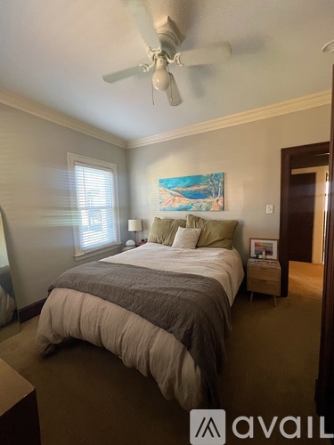 A bedroom with a bed, a ceiling fan, and a painting on the wall.
