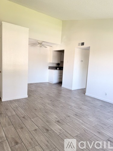A room with a wooden floor and white walls, with a door open to another room.