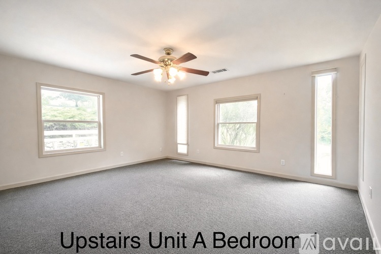 A bedroom with a ceiling fan and three windows.