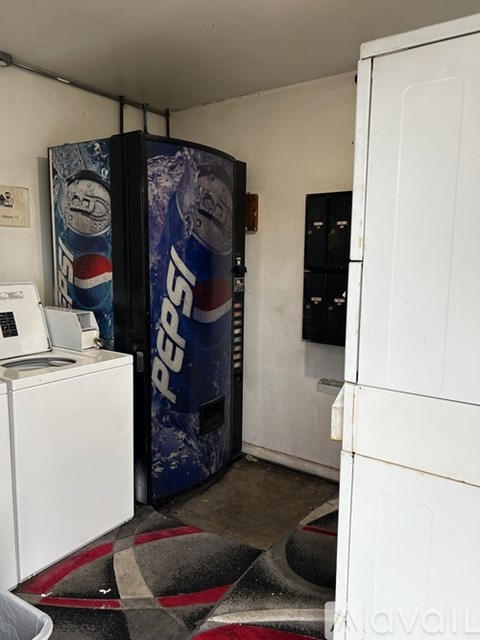 A Pepsi machine is in a room with a white fridge.