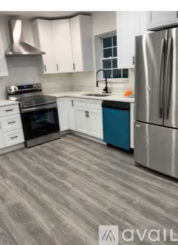 A kitchen with a stainless steel refrigerator, a stove, and a blue trash can.