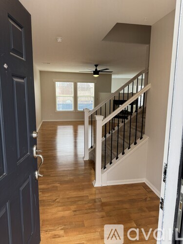 A hallway with a wooden floor, a staircase with black railings, and a ceiling fan.