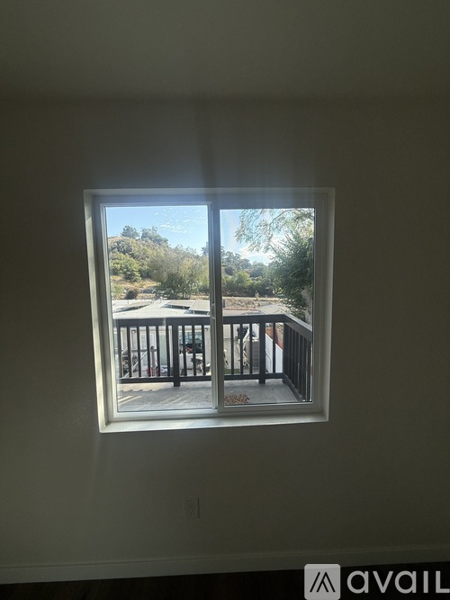 A window with a view of a balcony and trees outside.