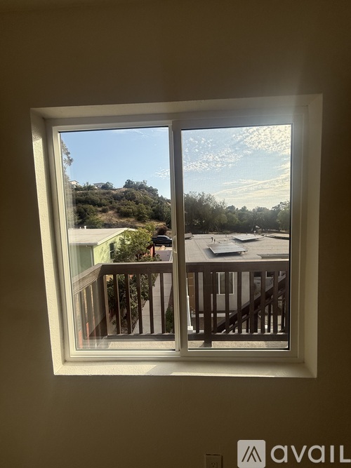 A window with a view of a balcony and trees outside.