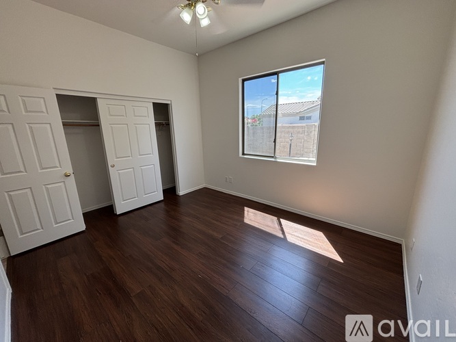 A room with wooden floors and a window showing a view of a building and a fence.
