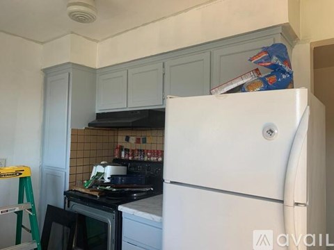 A kitchen with a white fridge, a black stove and a green step ladder.