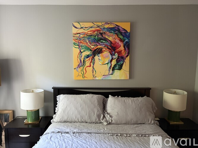 A bedroom with a large painting above the bed and two lamps on either side of the bed.