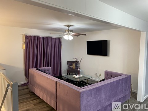 A living room with a purple couch and a flat screen TV mounted on the wall.