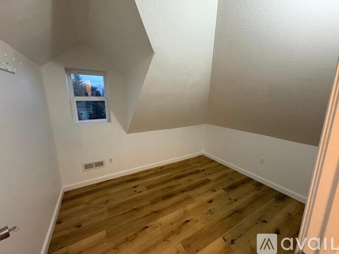A room with wooden flooring and a window showing a tree outside.