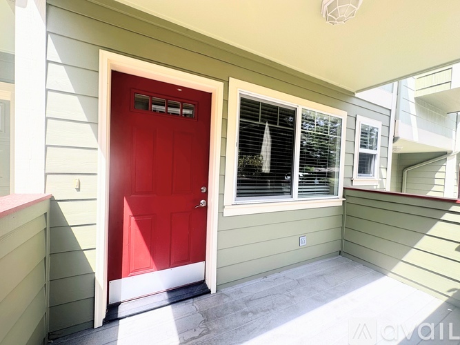 A red door is on the left side of a house with a window on the right.