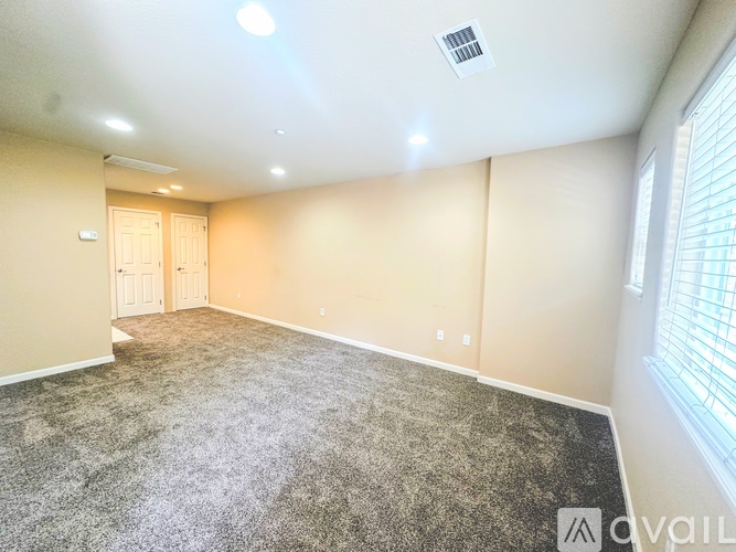 A spacious room with a carpeted floor and a window on the right side.