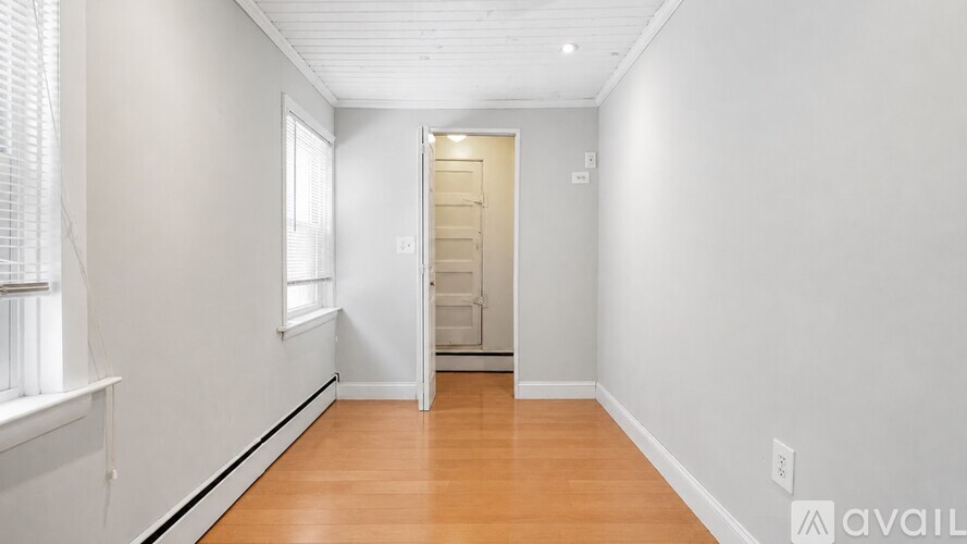 A room with a wooden floor and a white wall with a door in the middle.