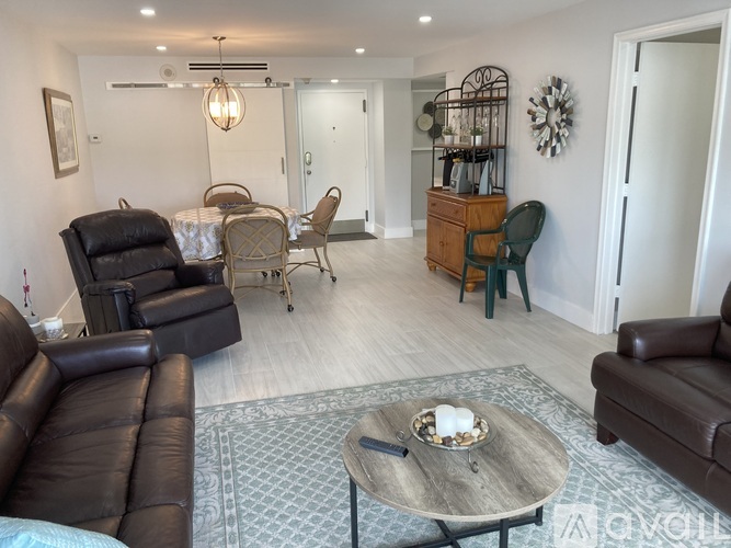 A living room with a brown leather couch, a wooden coffee table, and a dining table set up with chairs.