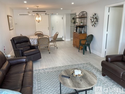 A living room with a brown leather couch, a wooden coffee table, and a dining table set up with chairs.