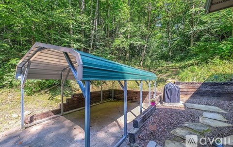 A covered patio area with a green roof and a fire pit surrounded by a gravel area and trees.