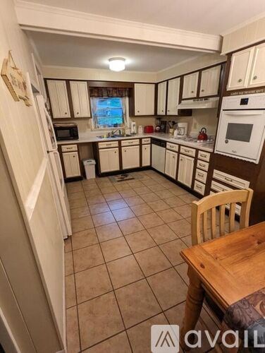 A kitchen with white cabinets and appliances, a wooden table and a window with a view of the outside.