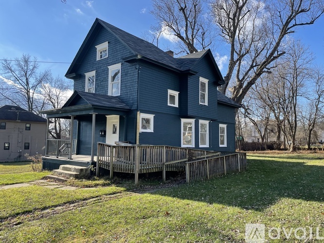 A blue house with a porch and a tree in the background.