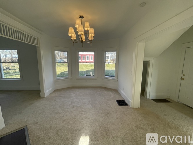 A room with a chandelier, carpeted floor, and a view of a red building through the windows.