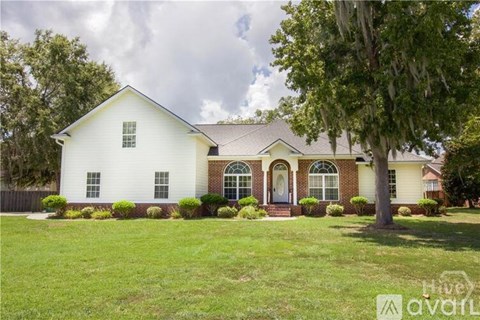 A white house with a brown roof and a tree in front.