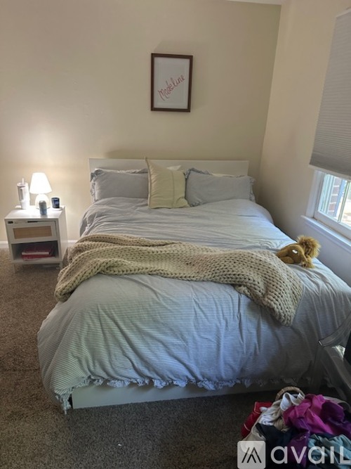 A bedroom with a bed, a teddy bear, and a nightstand with a lamp.