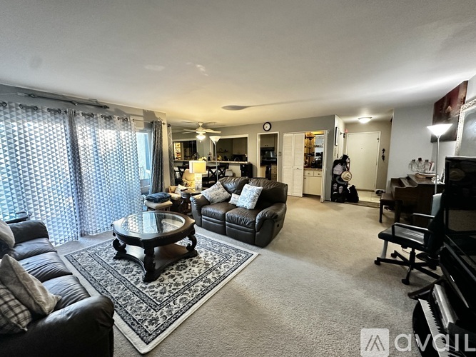 A living room with a black leather couch, a coffee table, and a piano.