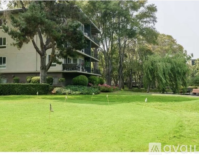 A grassy area in front of a building with trees and bushes.