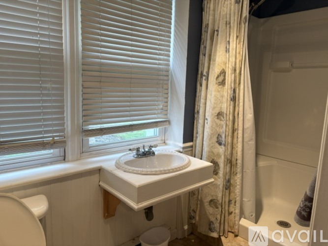 A white sink in a bathroom with a toilet and a window with blinds.