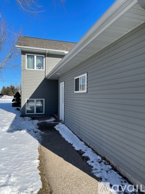 A house with a grey siding and a white door is shown with snow on the ground.