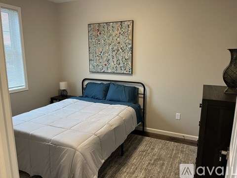 A bedroom with a bed, a painting on the wall, and a vase on a dresser.