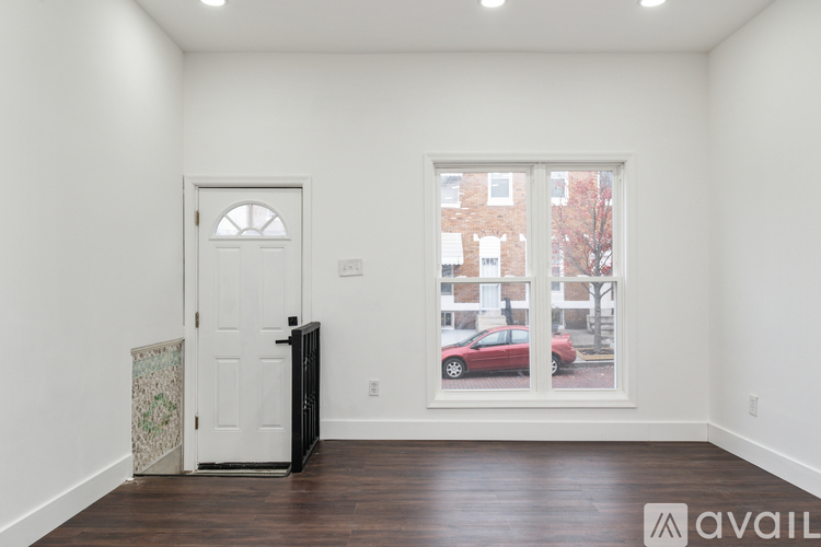 A room with a white door and a window showing a red car and a building outside.