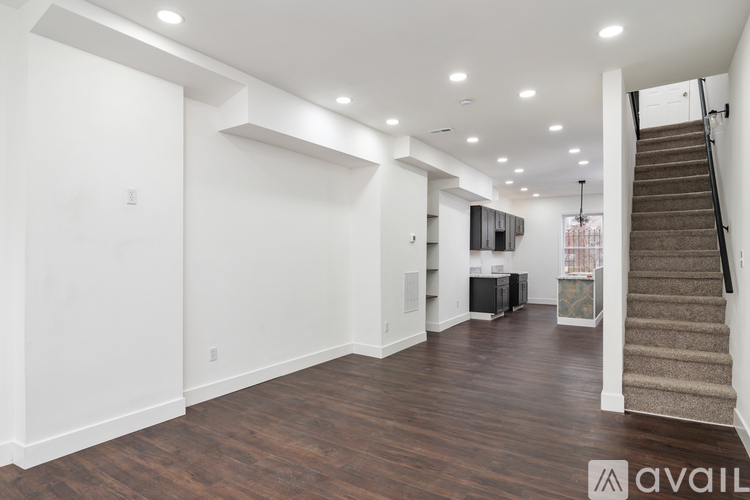 A spacious living room with wood flooring and a staircase on the right side.