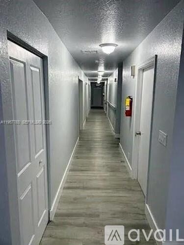 A long, narrow hallway with doors on both sides and a fire extinguisher in the distance.