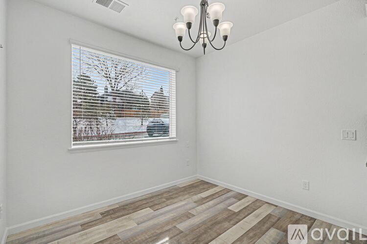 A room with a chandelier, wooden flooring, and a window with blinds.