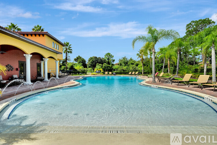 A large outdoor swimming pool with a yellow building and palm trees in the background.