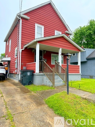 A red house with a porch and a trash can in front.