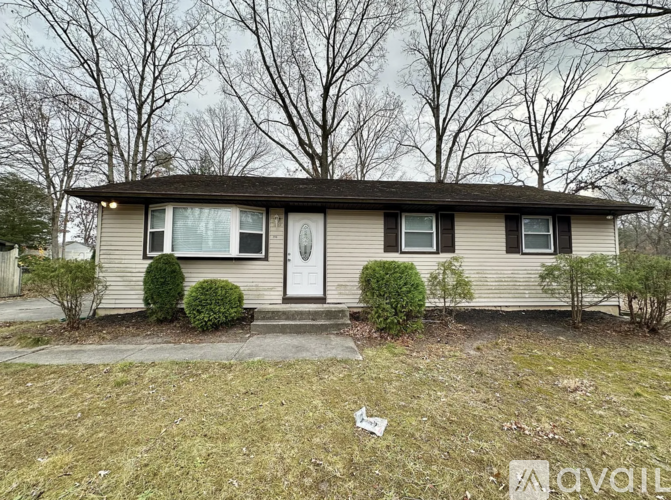 A house with a white door and windows is surrounded by trees.