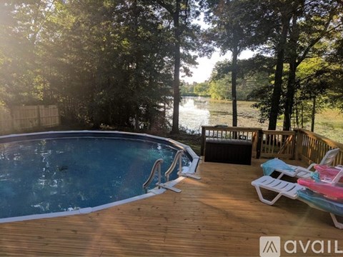 A pool with a sun lounger and a table is surrounded by trees.