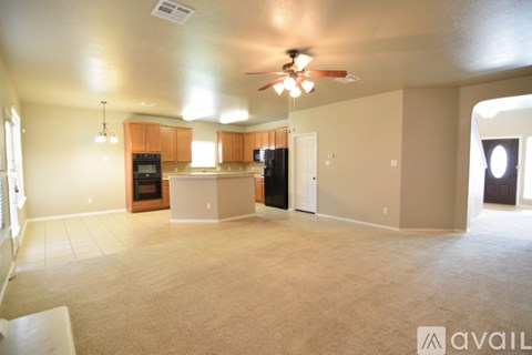 A spacious living room with a kitchen in the background and a carpet on the floor.