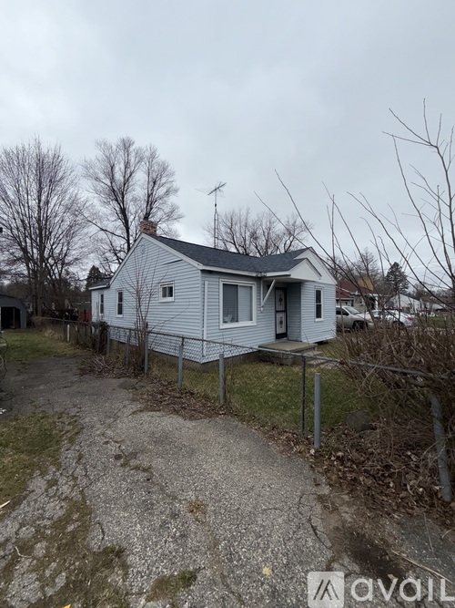 A small house with a grey roof and a gravel driveway in front.