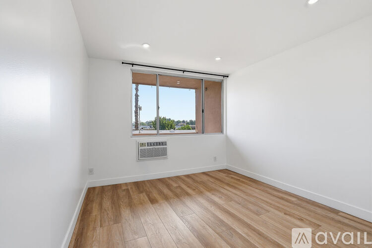 A room with wooden flooring and a window with a view of trees and a building outside.
