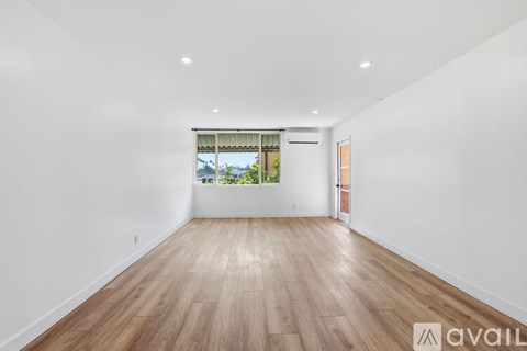 A spacious room with wooden flooring and a window overlooking a cityscape.