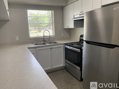 A kitchen with a stainless steel refrigerator and a window with blinds.