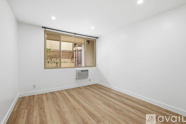 A room with wooden flooring and a window showing a view of a building.