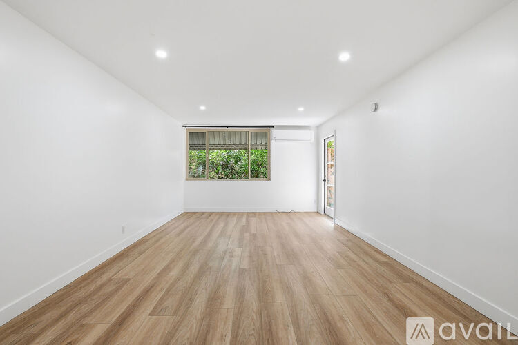 A spacious room with wooden flooring and a window with a view of greenery.