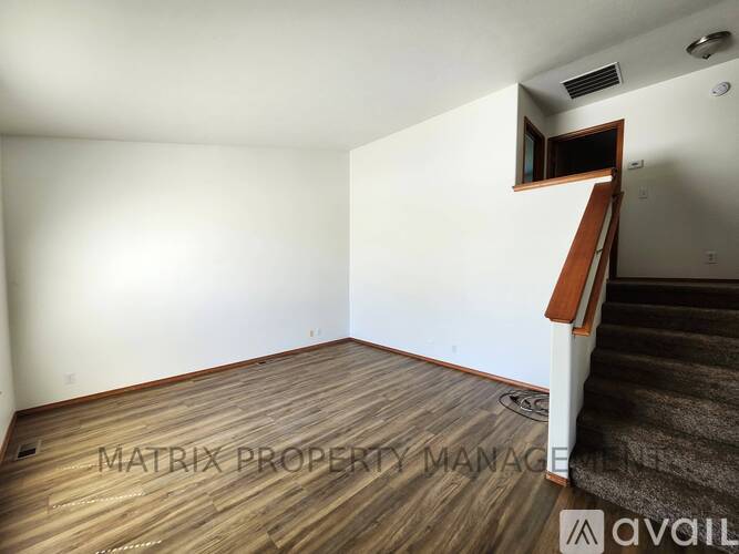 A room with wooden flooring and a staircase leading to another room.