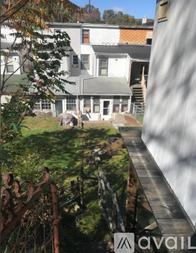 A house with a white exterior and a brown roof is surrounded by greenery.