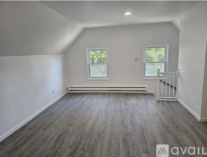 A room with wooden flooring and two windows.