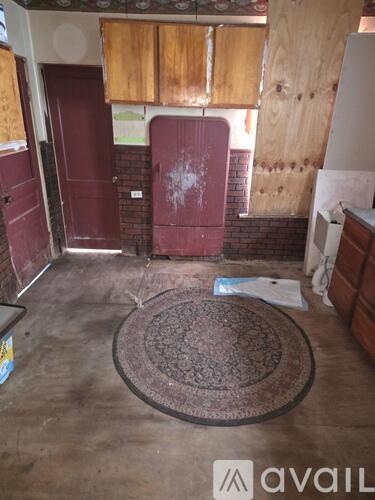 A room with a rug on the floor and a door with a red frame.