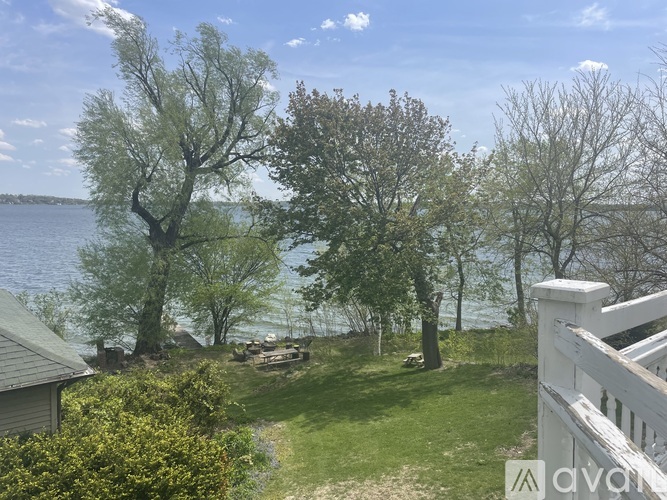 A white fence borders a grassy area with trees and a body of water in the distance.