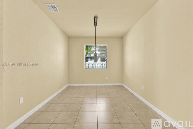 A room with beige walls and tiled flooring, featuring a window with blinds and a ceiling fan.